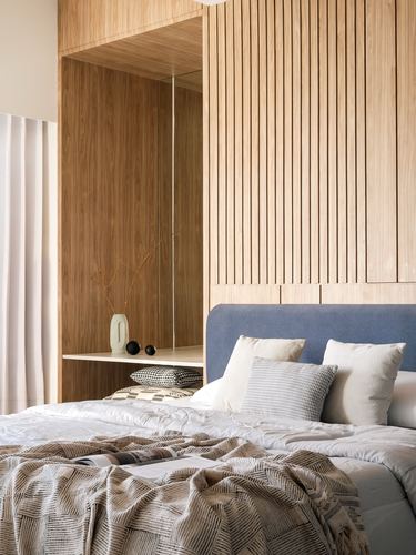 Bedroom with fluted wood wall, blue upholstered headboard, layered white and patterned linens