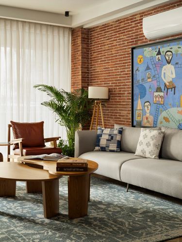 Living room with exposed brick wall, grey sofa, leather chair, and large colorful painting