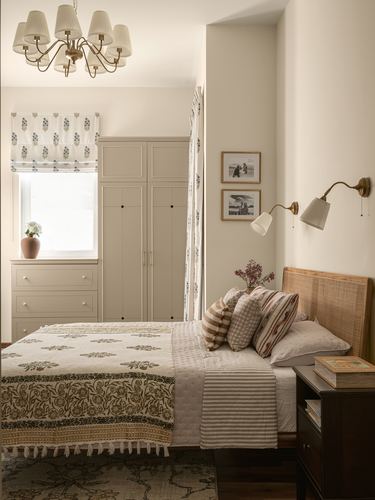 Bedroom with cane headboard, floral block-print bedding, wardrobe, and brass wall sconces