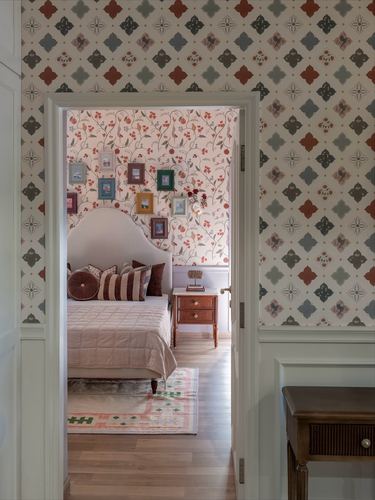 Doorway with geometric wallpaper opens into a bedroom with floral wallpaper and gallery frames