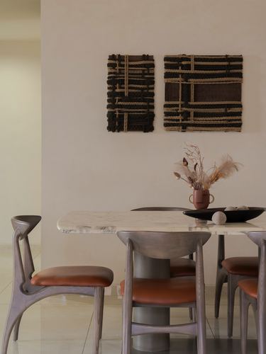 Dining table with marble top, curved wooden chairs, and woven wall art on a lime-plastered wall