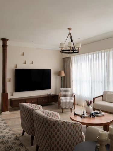 Living room with wall-mounted tv, wooden console, patterned armchairs and round coffee table under a chandelier