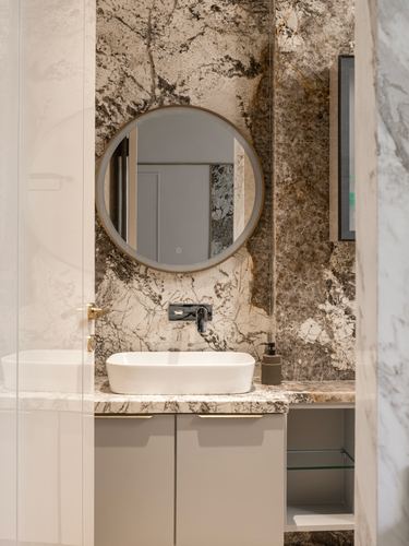 Bathroom with veined stone wall, round mirror, and vessel sink on stone-topped vanity