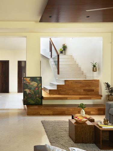 Living room with wooden staircase base, framed floral painting, and low wooden coffee tables on a grey rug