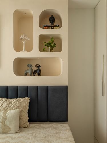 Beige plaster wall with curved recessed niches holding decor above a navy channel-tufted headboard