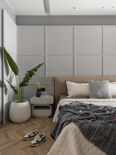 Neutral bedroom with paneled wall, upholstered headboard, patterned throw, plant and sneakers on herringbone floor.