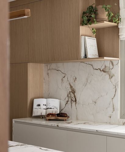 Kitchen corner with wood veneer cabinetry, veined stone backsplash, open cookbook and pastries on counter