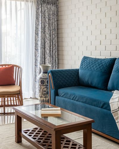 Living room corner with teal quilted sofa, cane armchair, wooden coffee table and brick-textured white wall