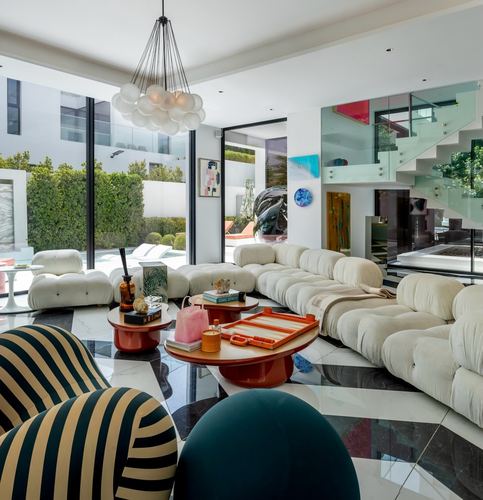 Living room with cream modular sofa, striped chair, orange tables and marble floor overlooking pool