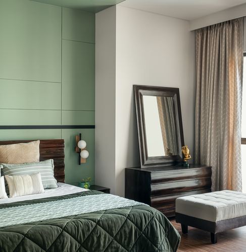 Sage green panelled bedroom with dark wood dresser, leaning mirror, and tufted bench