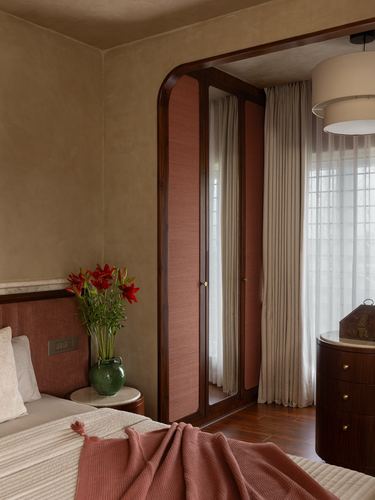 Bedroom corner with arched wardrobe, mirrored fabric doors, terracotta bedding and red lilies