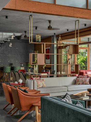 Living room with orange leather chairs, green velvet sofa, and a suspended brass-framed shelving divider.