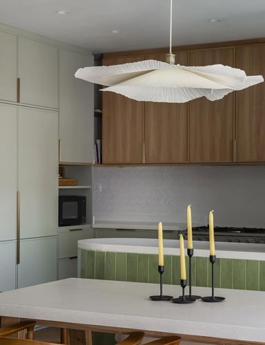 Kitchen with sage cabinets, wood upper units, curved green-tiled island, and sculptural pendant light
