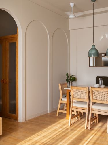 Sunlit dining nook with arched wall niches, cane chairs, and green pendant lights over a wooden table