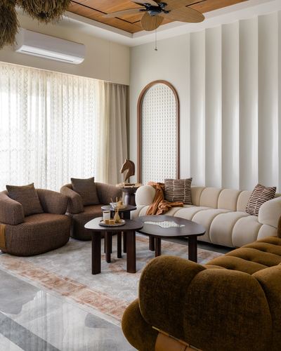 Living room with curved beige sofa, brown velvet chairs, and fluted wall paneling around an arched mirror