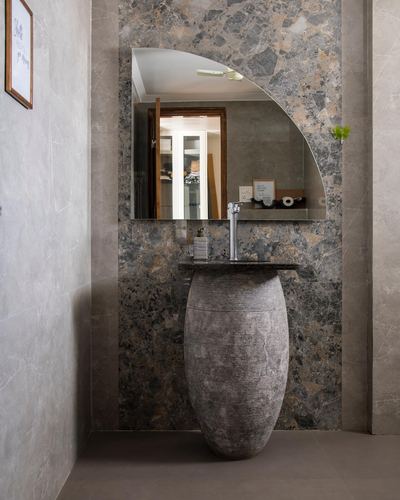 Stone-clad bathroom with urn-shaped pedestal basin and curved mirror reflecting a window