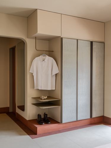 Wardrobe nook with fabric-panelled shutters, open shelf holding a shirt, terracotta step platform