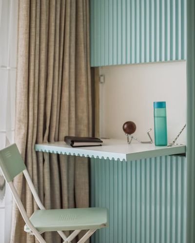 Mint fluted cabinet with fold-down scalloped desk, folding chair, and sheer curtain beside it