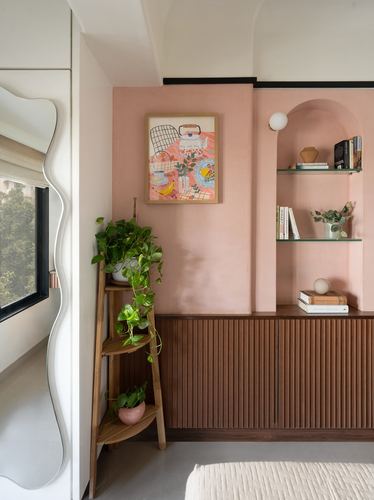 Pink lime-plastered wall with arched shelf niche, ribbed wood cabinet, wavy mirror and plant stand