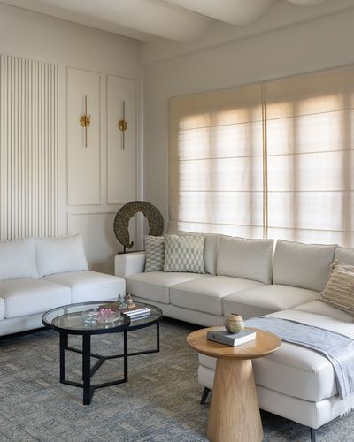 Beige L-shaped sofa with round glass and wood tables in a minimal living room with sheer curtains