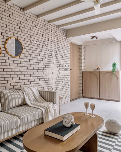 Living room with brick wall, striped sofa, oval wood coffee table and arched wooden cabinet