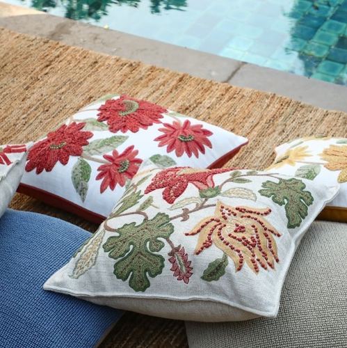 Floral embroidered cushions arranged on a jute mat beside a tiled pool edge