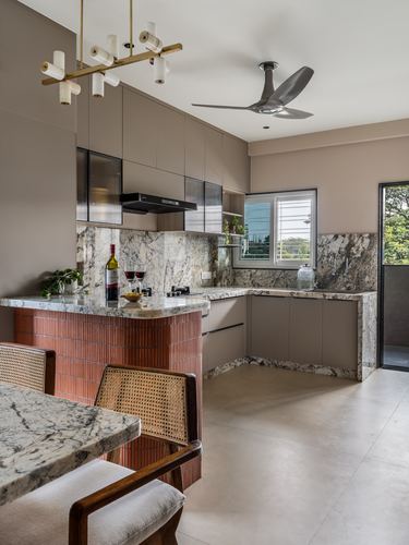 L-shaped kitchen with stone countertops, terracotta-tiled island, and brass pendant lighting