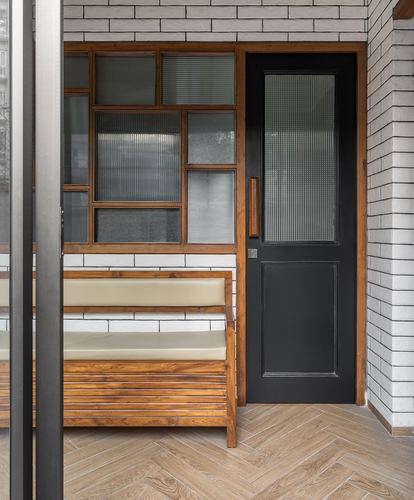 Entryway with wood-framed fluted glass window grid, black door, and built-in wooden bench on herringbone floor