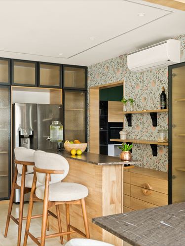 Wood kitchen with floral wallpaper nook, open shelves, stone counter and cane bar stools