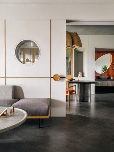 Living room with sliding paneled wall featuring round window, opening to dining and orange-tiled kitchen beyond