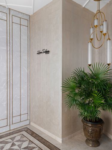 Beige paneled foyer corner with potted palm, brass chandelier, and marble inlay floor