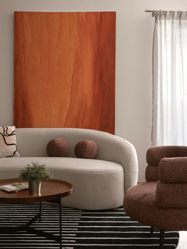 Curved cream sofa beneath a large orange abstract painting, with a striped rug and tufted ottoman