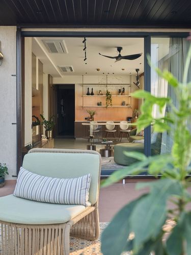 Terrace lounge chair framed by foliage looking through open glass doors into a warm-toned living and dining space