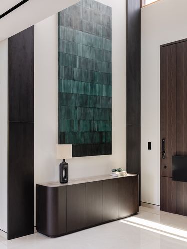 Entry foyer with dark wood panels, textured green ceramic wall art, and curved console cabinet