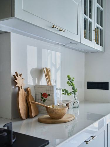 White kitchen counter styled with wooden bowls, utensil holders and a small glass vase of greenery