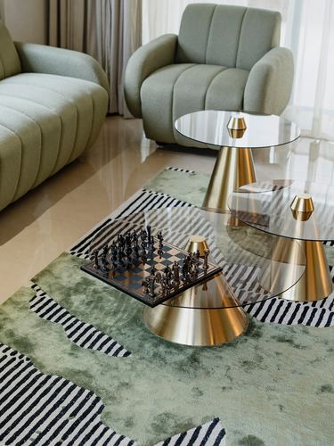 Sage boucle sofa and armchair around brass-and-glass nesting tables with chess set on patterned rug
