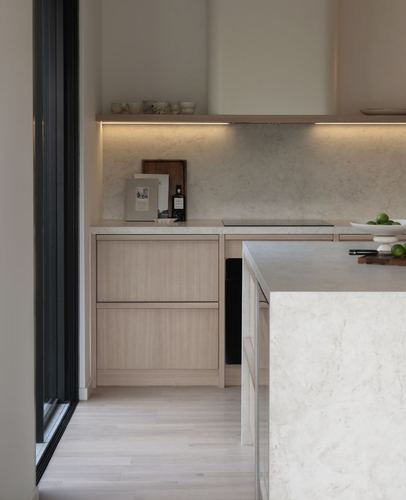 Minimalist kitchen with waterfall stone island, wood cabinetry, and warm under-cabinet lighting