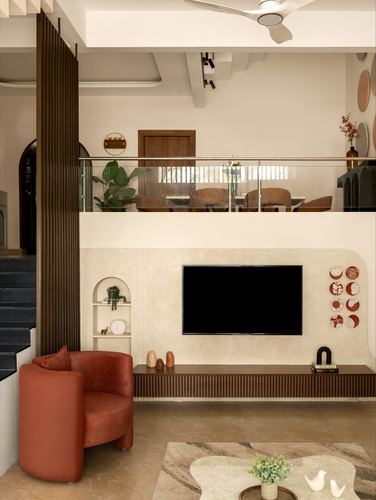 Double-height living room with fluted wood pillar, terracotta chair, and mezzanine dining area above