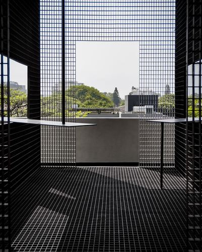 Mesh-clad architectural passage with square opening framing trees and rooftops beyond