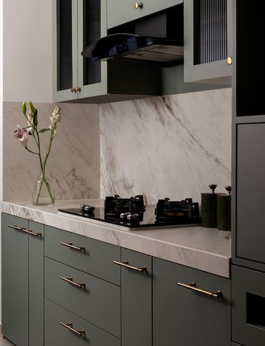 Sage green kitchen cabinetry with marble countertop, backsplash, gas hob and brass handles