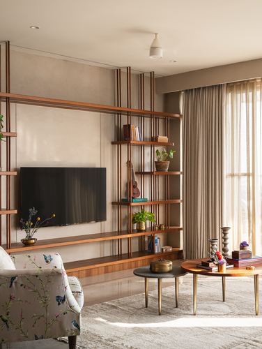 Living room with open wood shelving, wall-mounted tv, floral armchair, and nested coffee tables in warm daylight