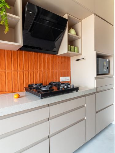 Beige kitchen counter with black hob under chimney hood against ribbed orange tile backsplash