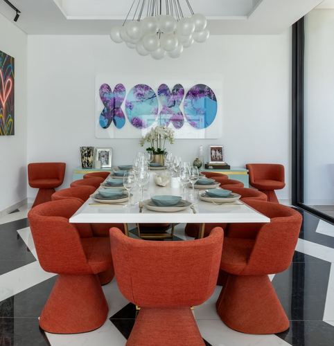 Dining room with ten orange barrel chairs around a white marble table under a globe chandelier