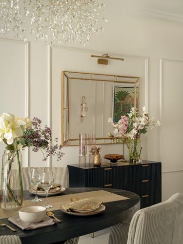Dining room with black fluted sideboard, gilt mirror, chandelier, and floral table setting