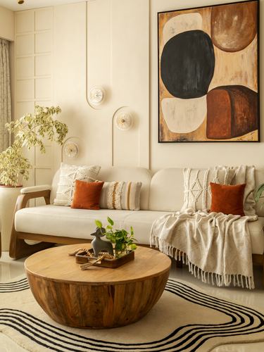 Beige living room with wooden sofa, rust cushions, round wood coffee table, and abstract painting above.