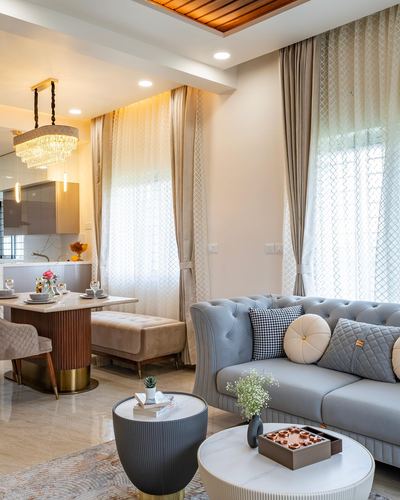 Open living and dining area with blue tufted sofa, crystal chandelier, and layered curtains
