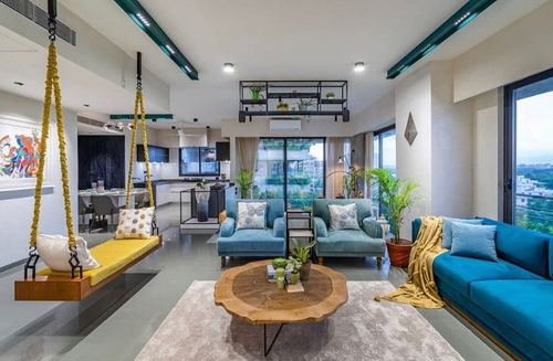 Open-plan living room with teal sofas, wooden swing, round coffee table and kitchen beyond