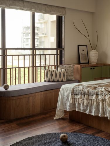 Wooden window seat with cushions beside a bed and green cabinet in a warm-toned bedroom