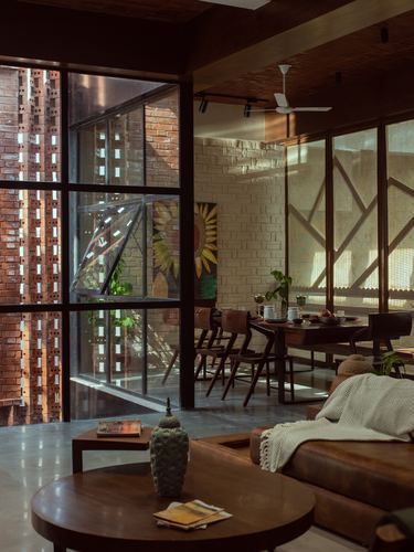Living and dining space with exposed brick, wood furniture, and glass wall opening to a brick facade at golden hour