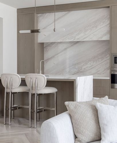 Neutral-toned kitchen with marble backsplash, wood cabinetry, and boucle bar stools beside a cream sofa